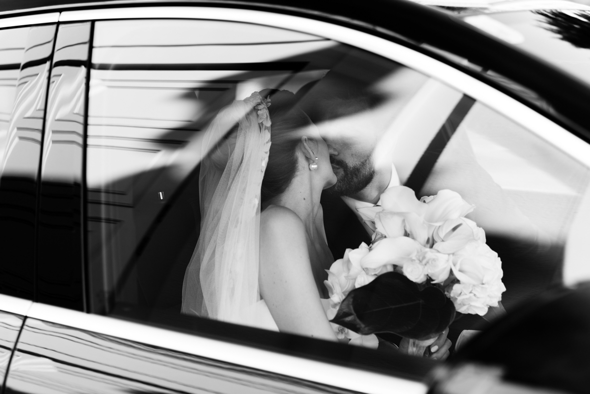 Wedding Photographer Austria — Brautpaar Kuss durch Auto-Fenster mit Schleier in Schwarzweiß