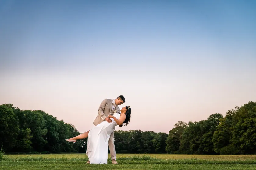 A photo showing the groom holding the bride in his arms and tilting her backwards as the sun sets on the horizon.