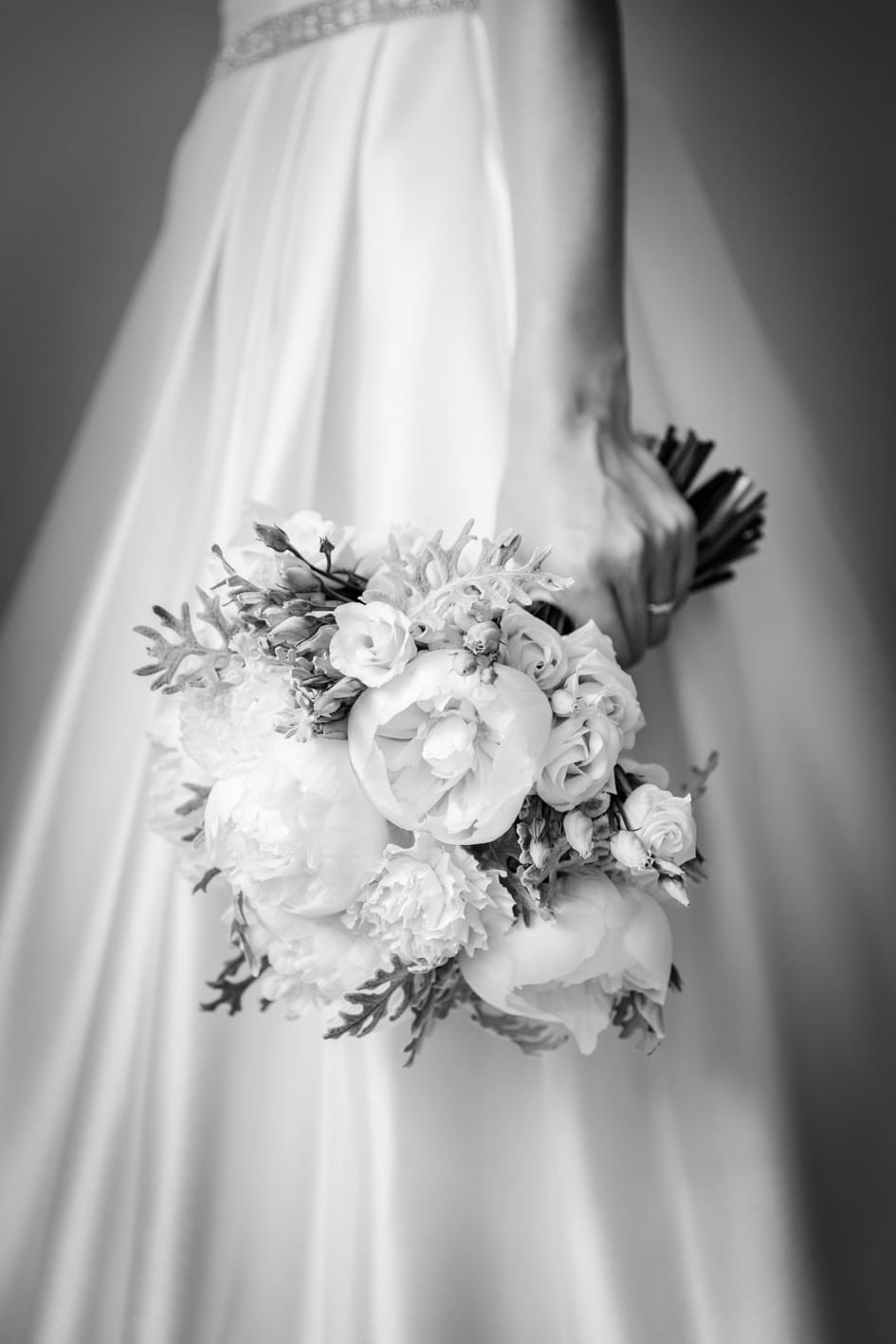 Hochzeitsfotograf — Brautstrauß mit Pfingstrosen vor Brautkleid in Schwarz-Weiß